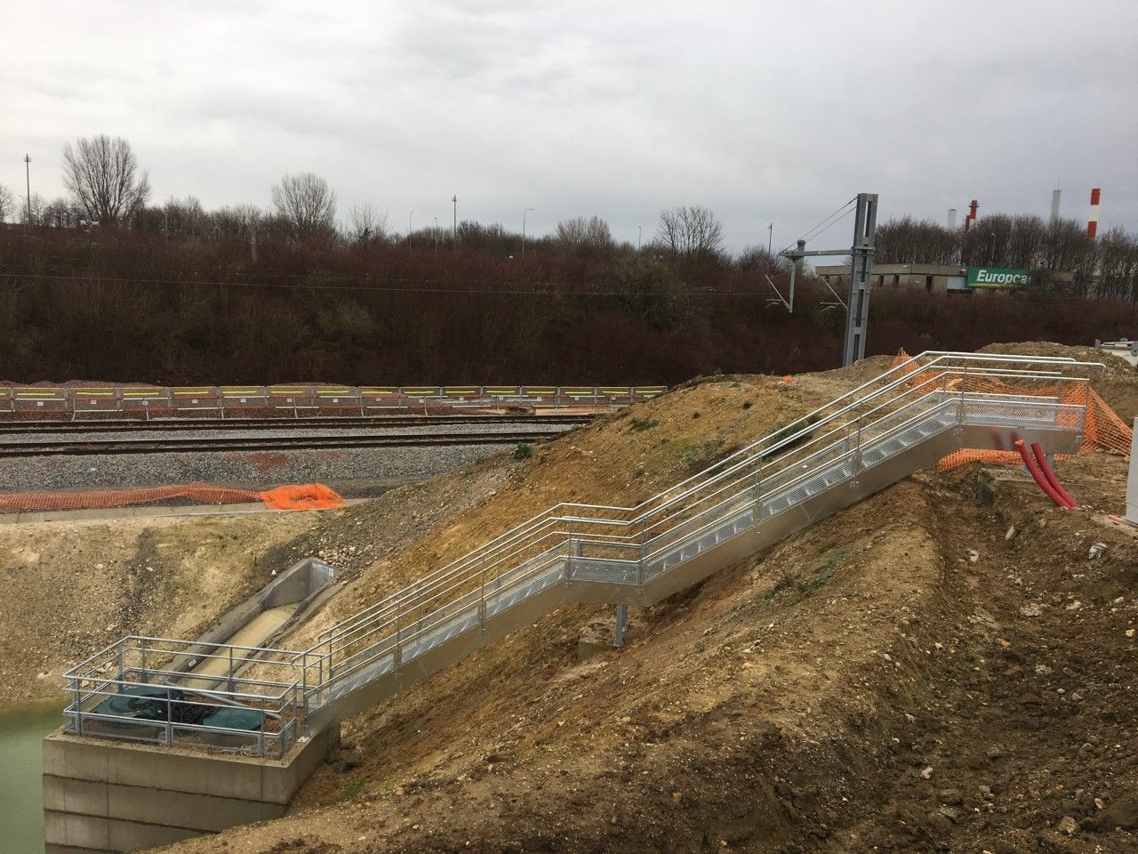 Escalier en béton en construction sur un talus herbeux près des voies ferrées