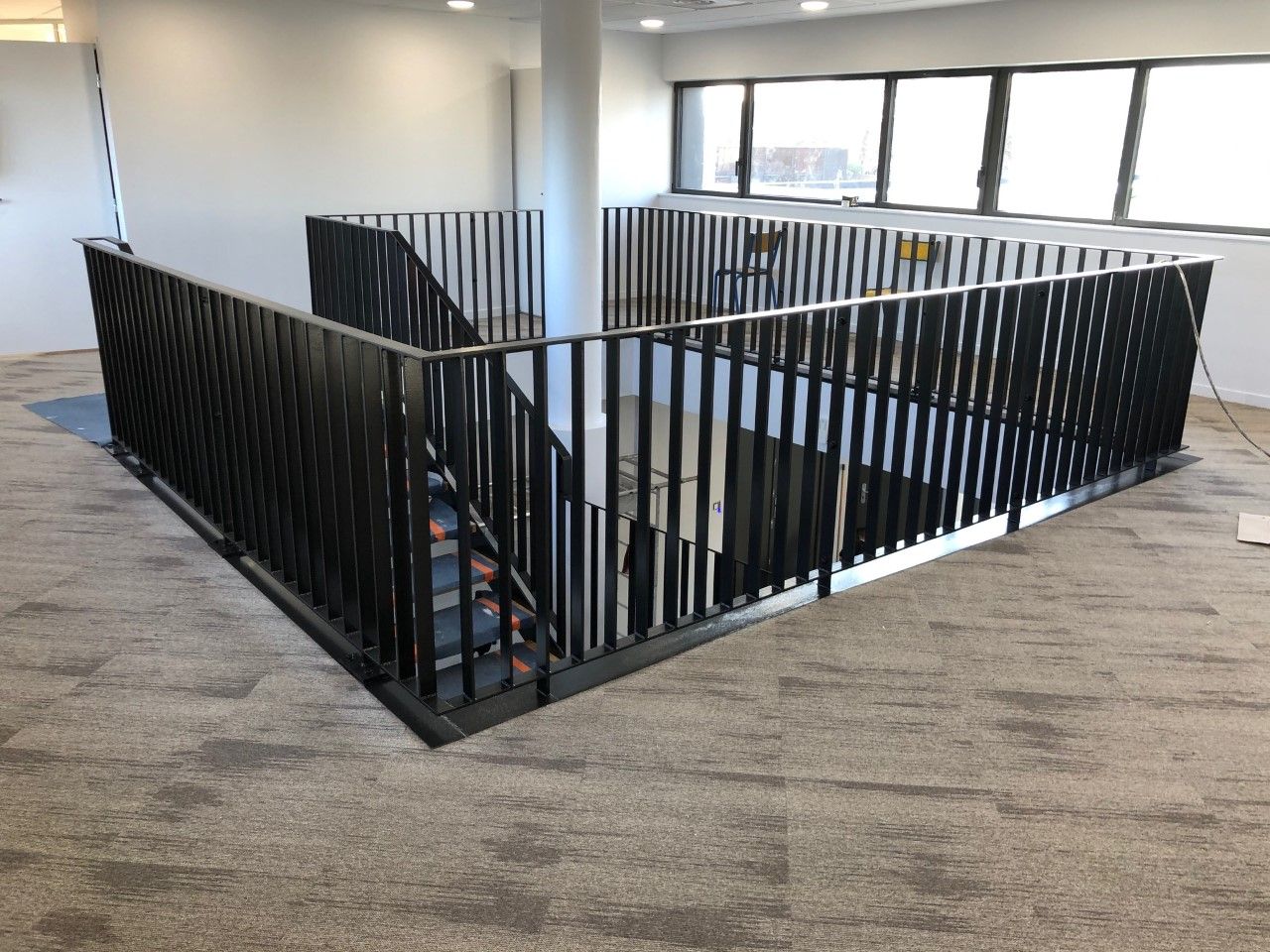 Espace de bureau intérieur avec des rampes en métal noir autour d'une cage d'escalier ouverte sur moquette au sol