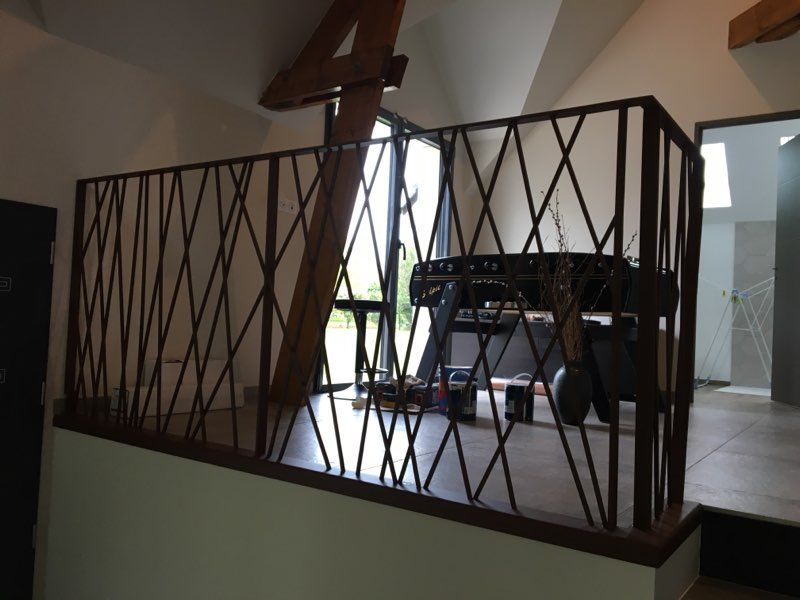 Balcon intérieur avec rambarde en métal noir et table sur un sol carrelé, donnant sur un extérieur lumineux.