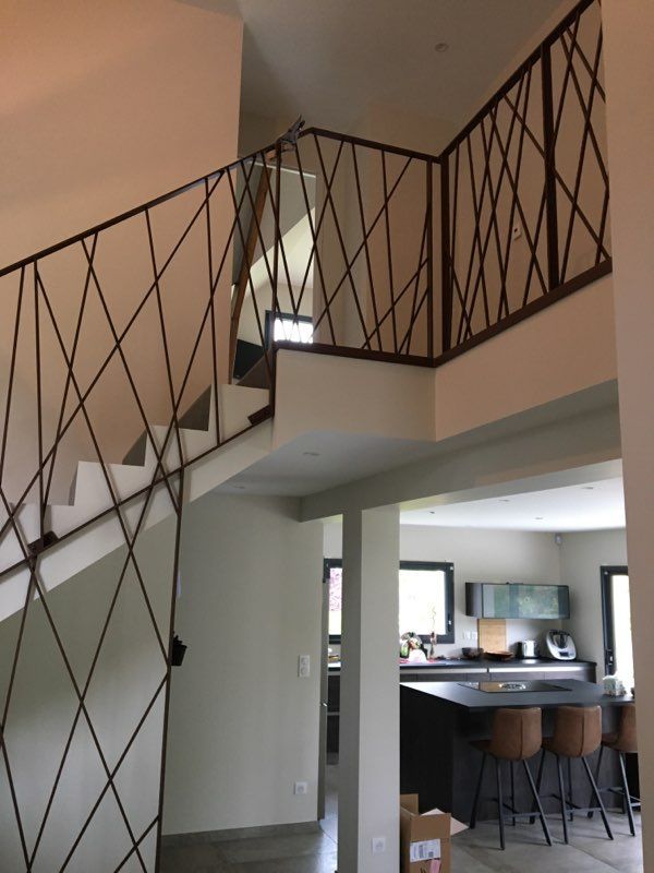 Palier d'escalier intérieur avec rambarde noire à croisillons donnant sur une cuisine et une salle à manger en contrebas.