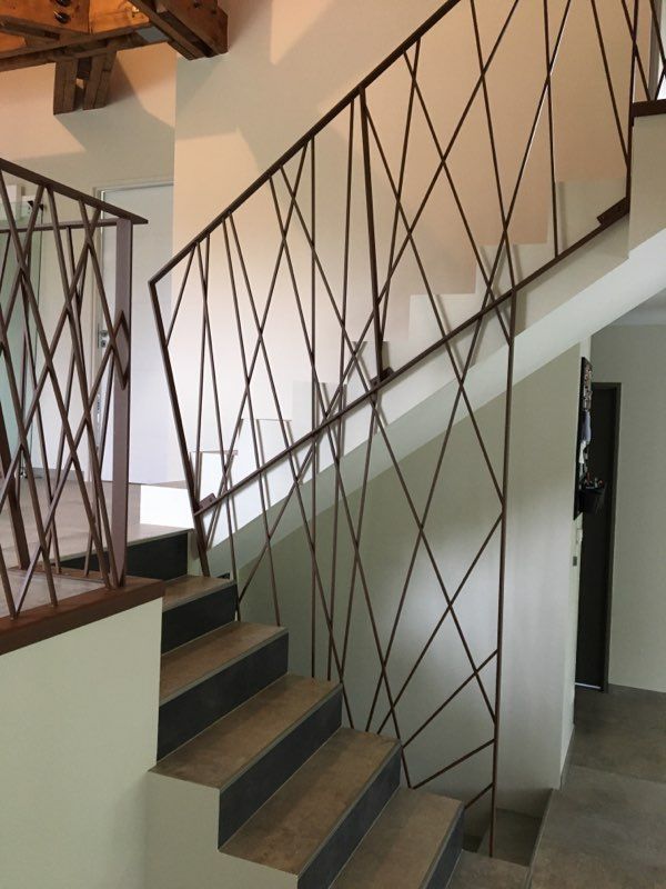 Escalier intérieur avec marches sombres et rampe métallique décorative à croisillons.