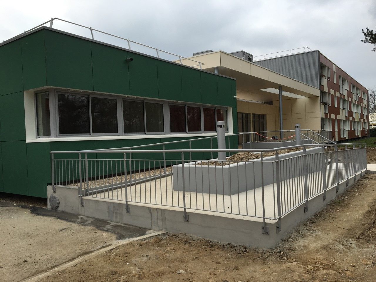 Bâtiment vert et beige avec rampe d'accès pour fauteuil roulant et rambardes extérieures