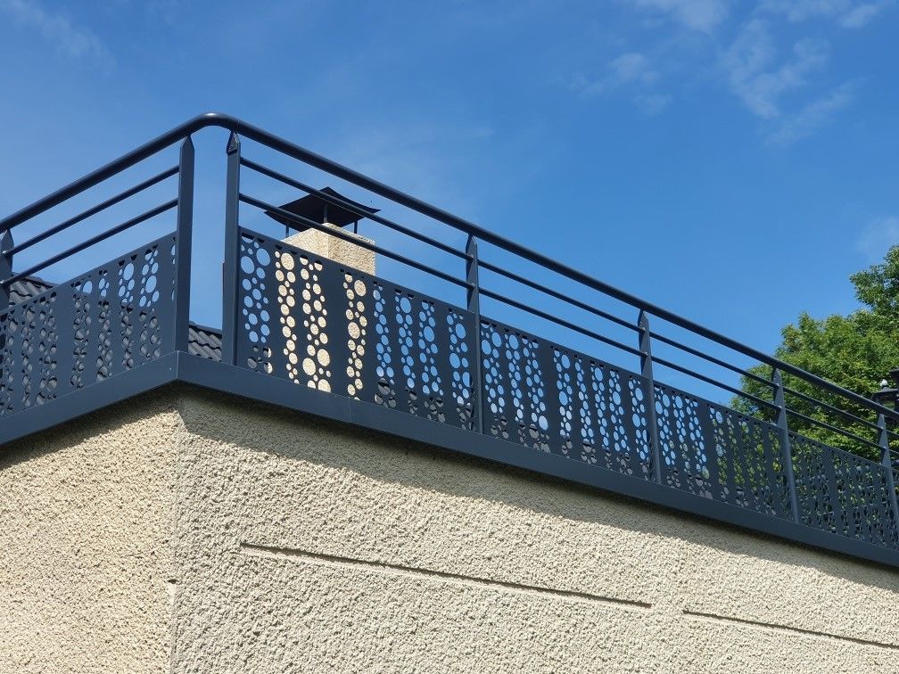 Rambarde de toit en métal bleu au sommet d'un bâtiment beige se détachant sur un ciel bleu clair