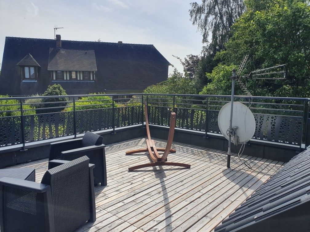 Terrasse sur le toit avec chaises en osier noir, table en bois et antenne parabolique blanche au soleil
