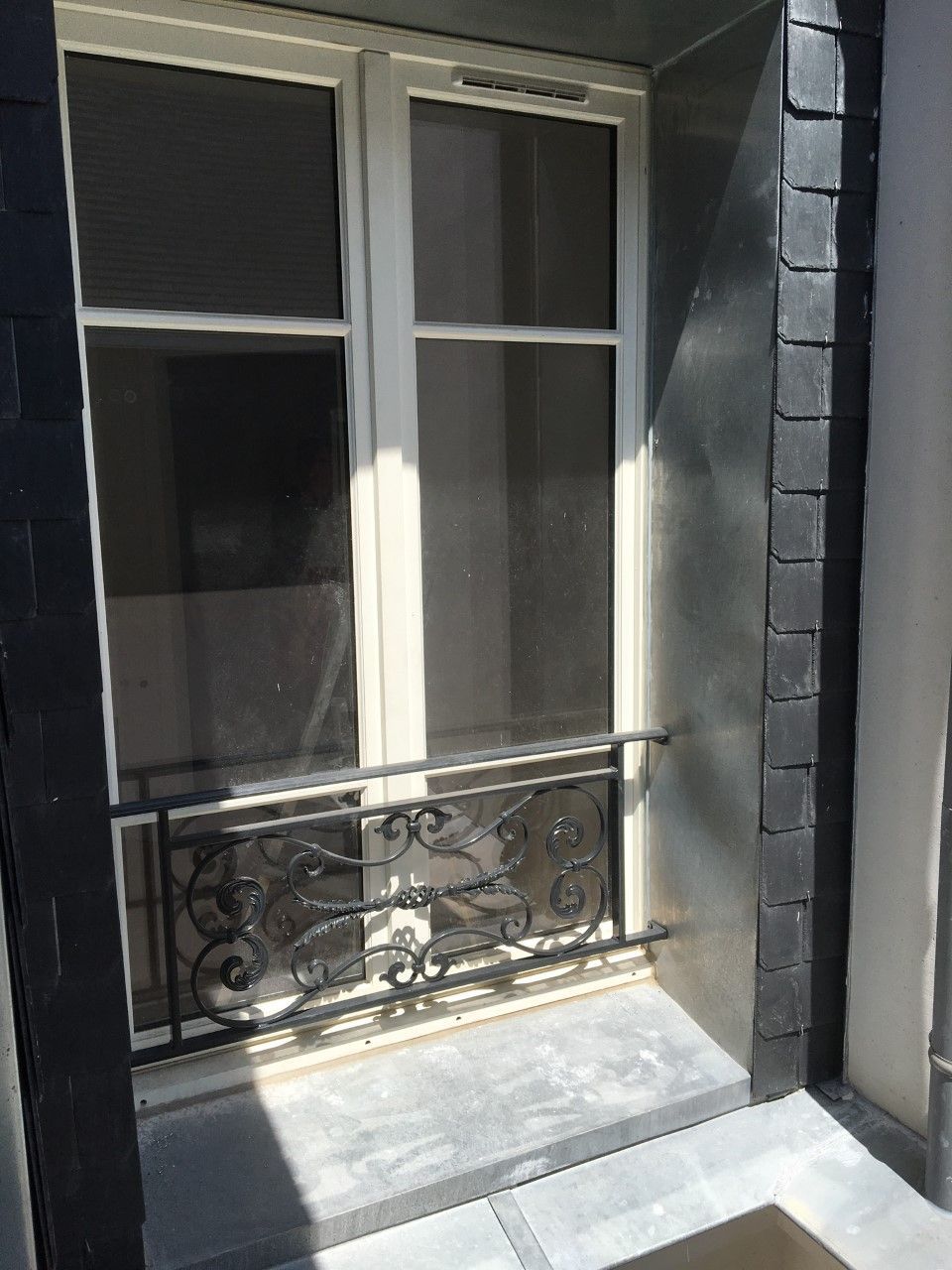 Fenêtre ensoleillée avec balustrade décorative noire sur un mur extérieur sombre
