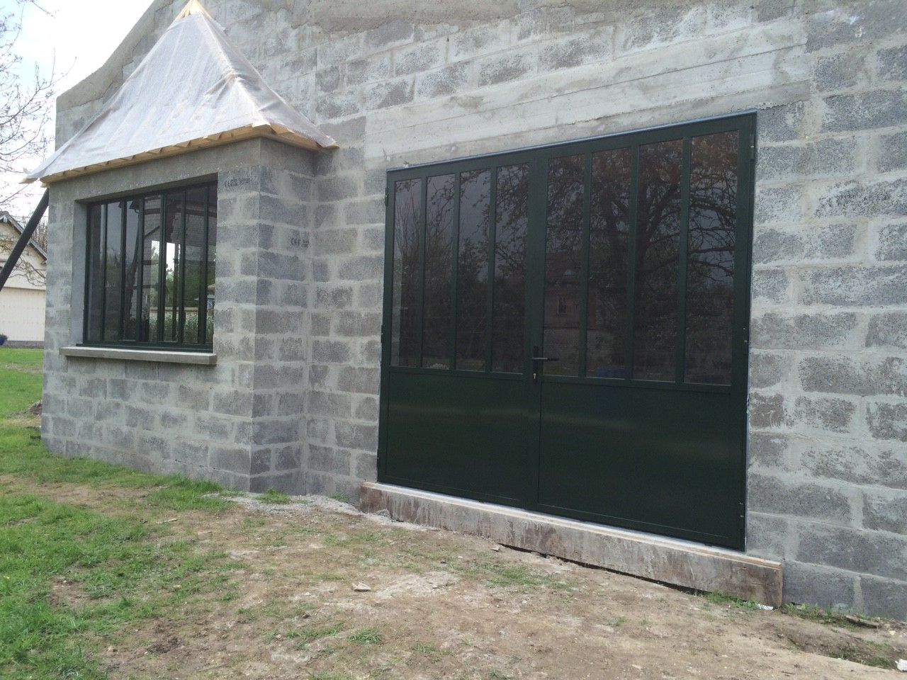 Façade en pierre d'un bâtiment avec de grandes fenêtres teintées foncées et un petit espace vert au premier plan.