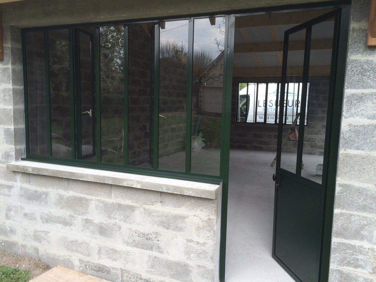 Porte ouverte et fenêtres à cadre vert sur l'extérieur d'un bâtiment en parpaings