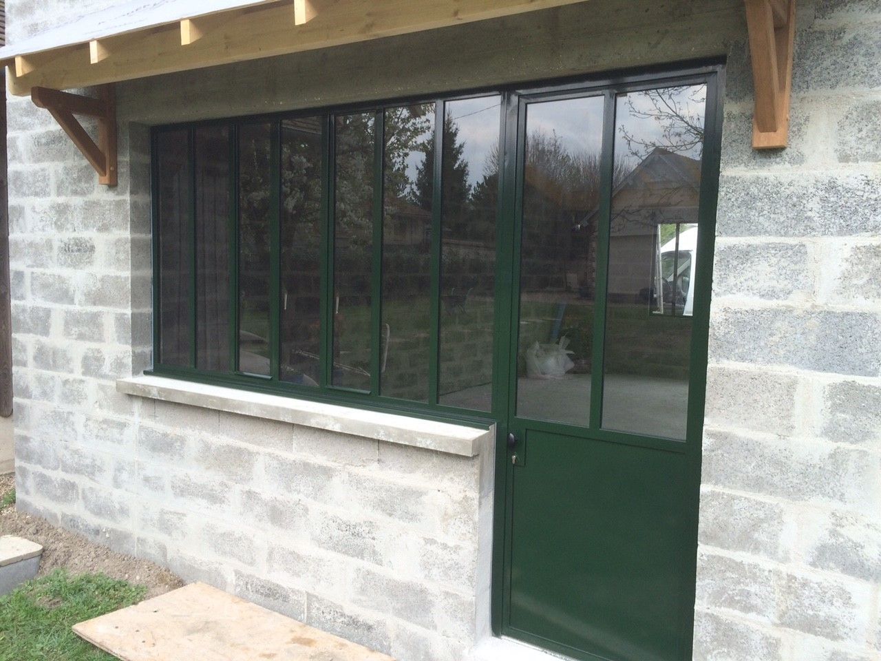 Porte et fenêtres en verre vert sur la façade en pierre d'un bâtiment sous un auvent.
