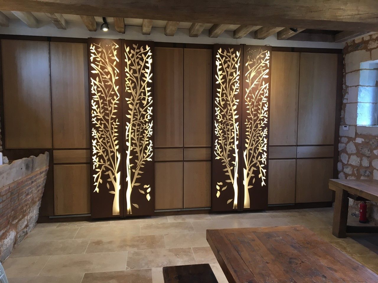 Pièce rustique avec mur lambrissé, panneaux décoratifs lumineux en forme d'arbre, éléments en pierre et grand tapis.