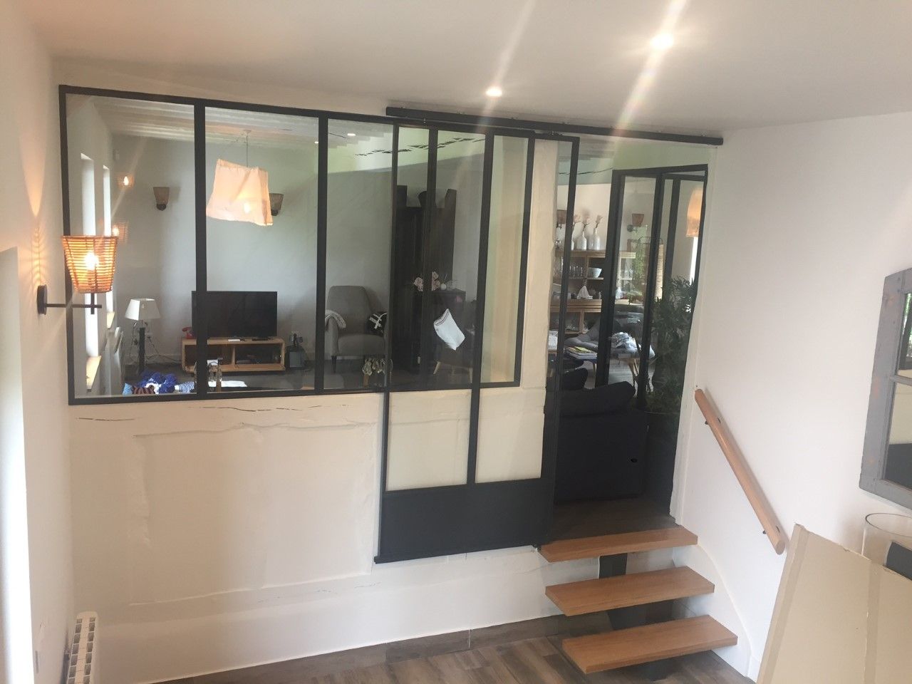 Intérieur de loft moderne avec cloison vitrée à cadre noir, escalier en bois suspendu et télévision murale