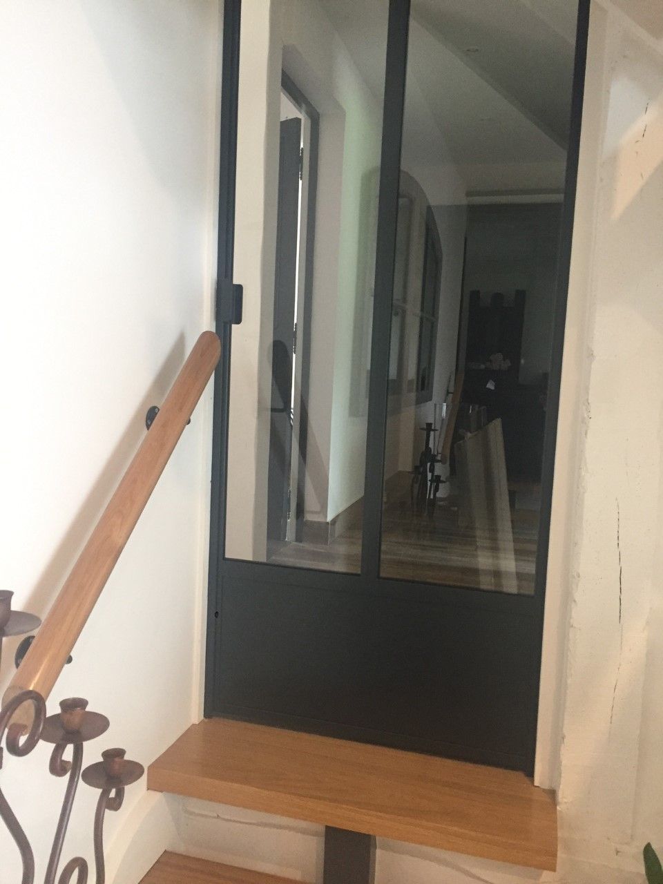 Escalier avec marches en bois, porte vitrée à cadre noir et reflet d'un couloir avec un petit chien.