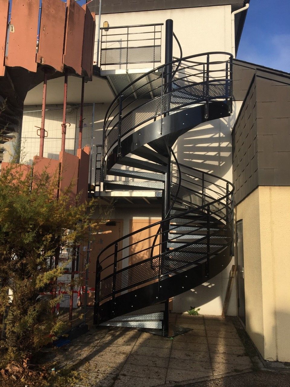 Escalier de secours en colimaçon noir sur le côté d'un bâtiment, en plein jour.