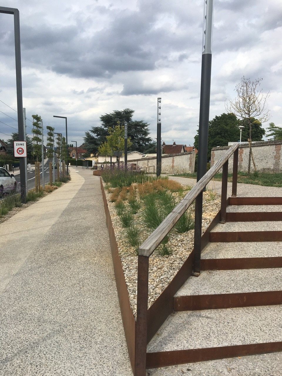 Allée pavée tranquille longeant des escaliers bruns et des aménagements paysagers sous un ciel nuageux