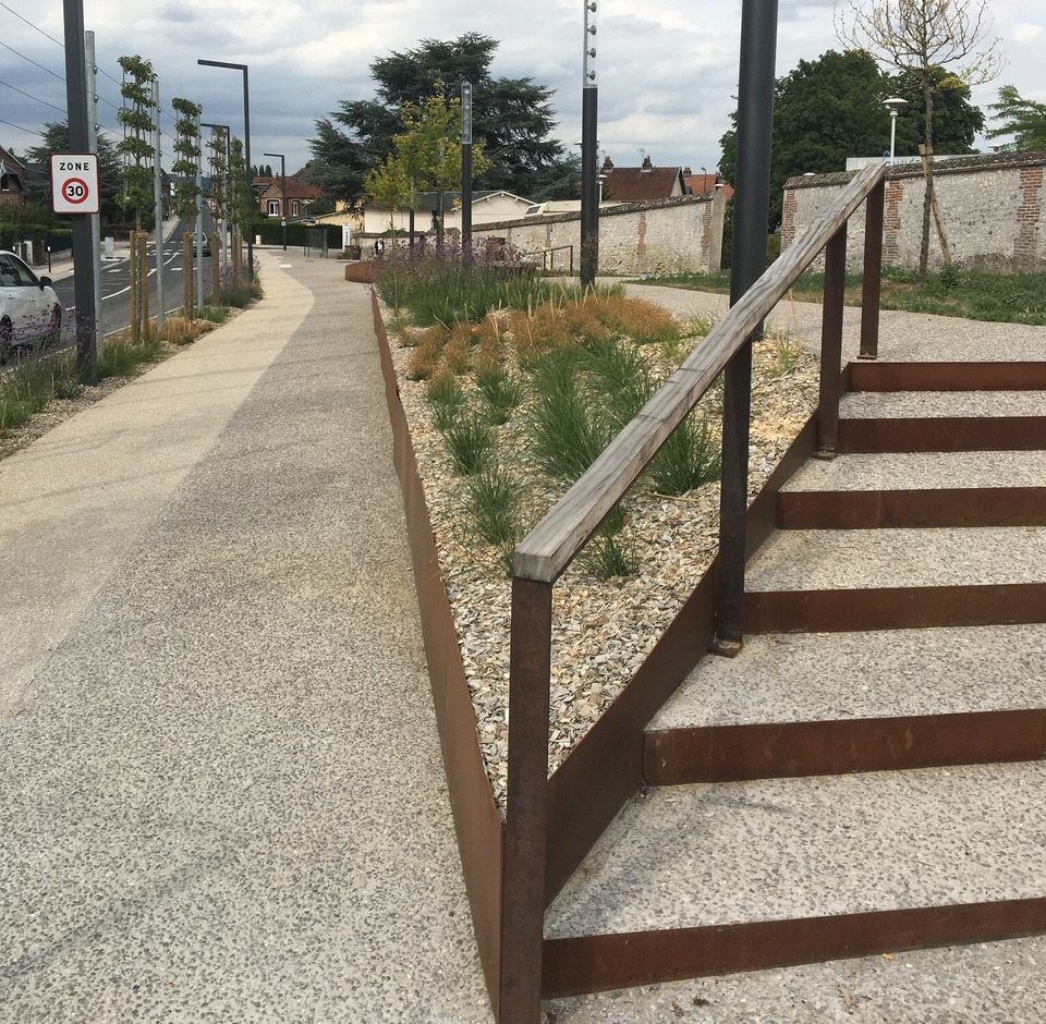 Allée en béton longeant un escalier à rampes métalliques dans un quartier résidentiel calme