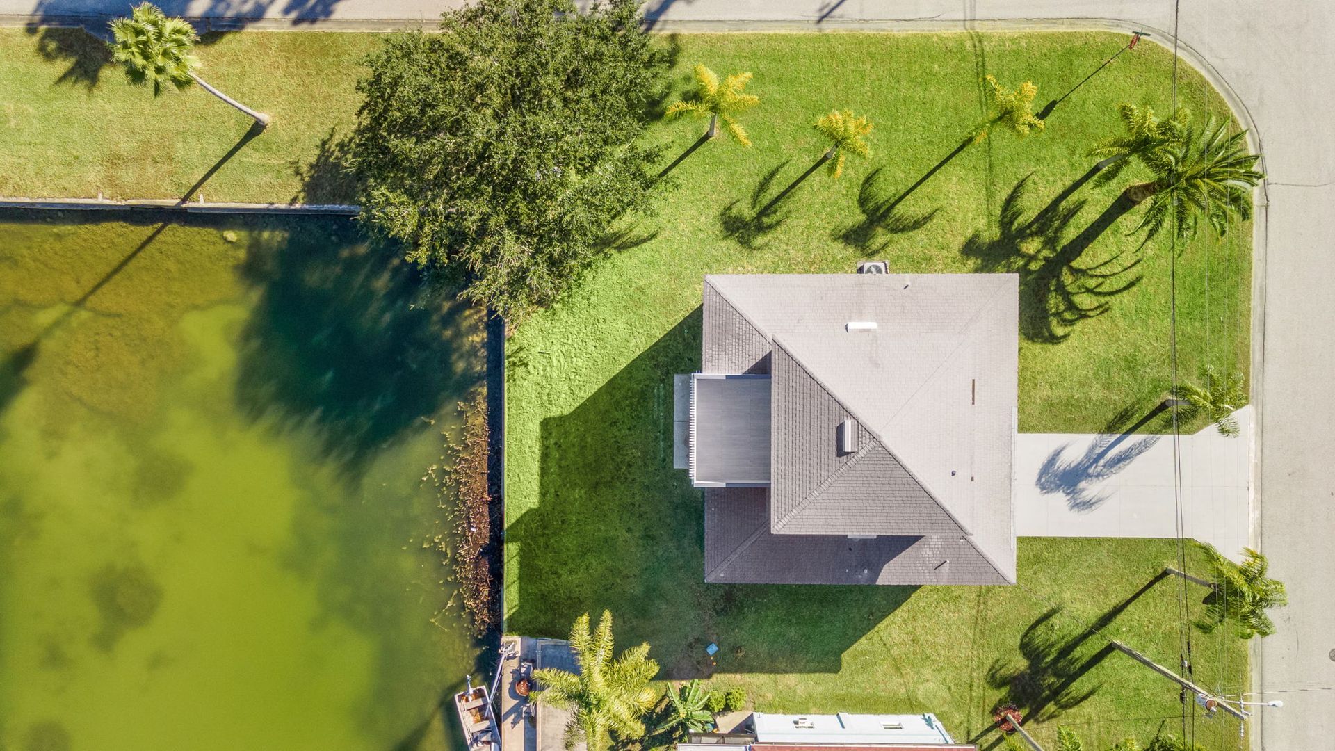 Aerial view of a house beside a green lawn and canal with trees and a driveway