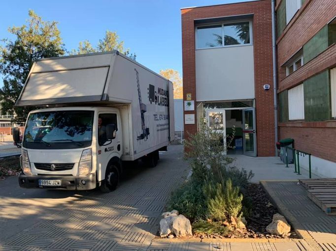 Camión de mudanzas blanco estacionado frente a la entrada de un edificio de ladrillo.