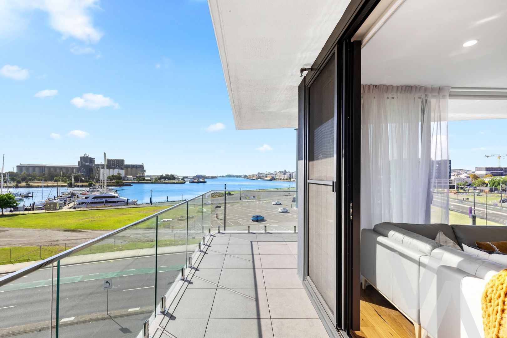 A balcony view overlooking a harbor with a building, greenery, and water under a clear blue sky.