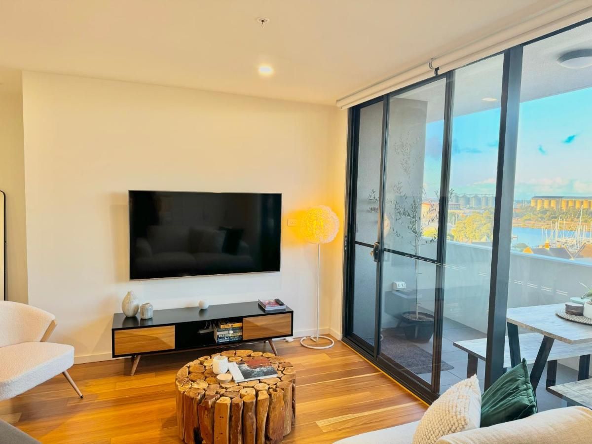 Modern living room with a mounted flat-screen TV, wooden console, textured log coffee table, and sliding glass balcony door.