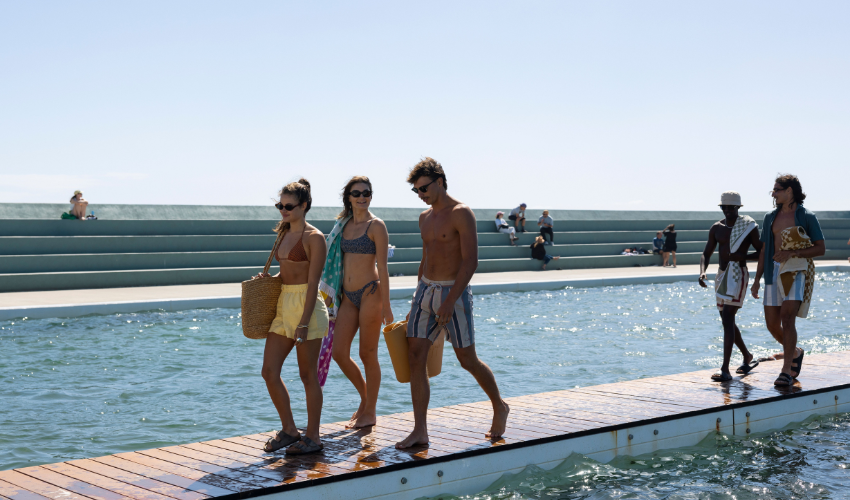 People in swimwear walk along a pool's edge in bright sunlight. Newcastle NSW