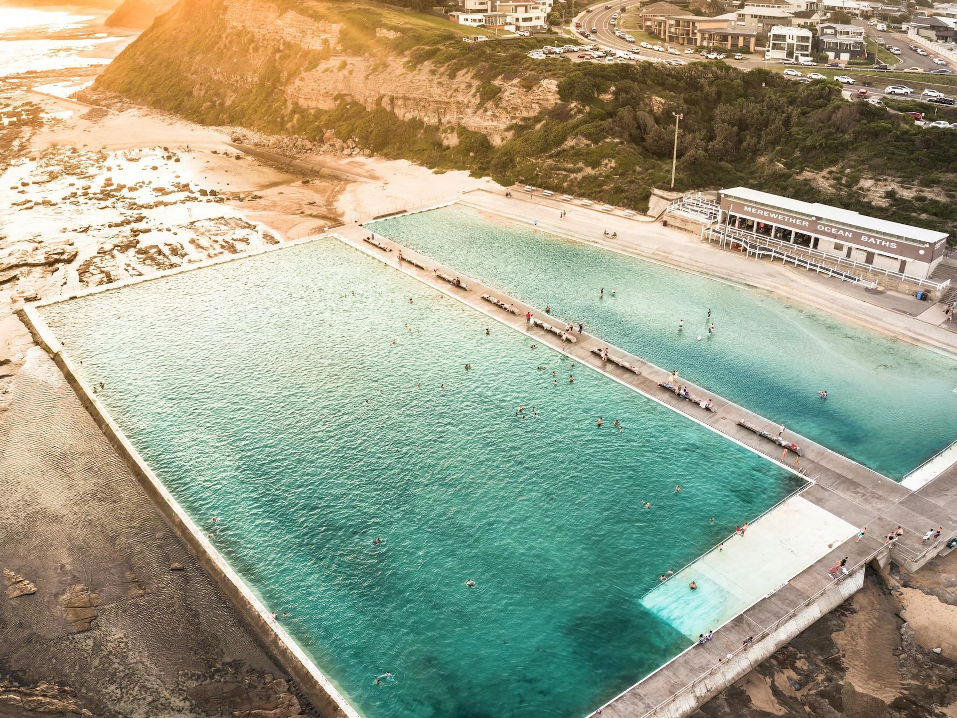 Aerial view of ocean pools with turquoise water, adjacent to a beach and buildings. Newcastle NSW