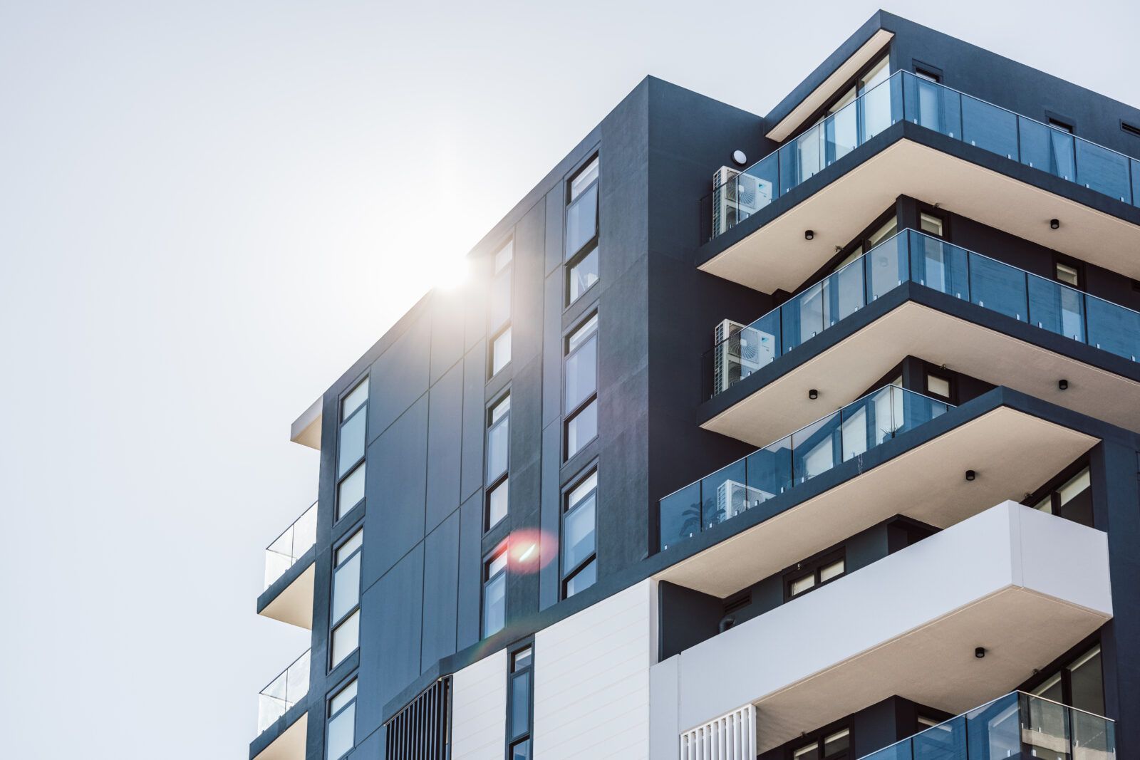 A low-angle view of a modern multi-story apartment building with dark gray exterior walls and glass balcony railings.