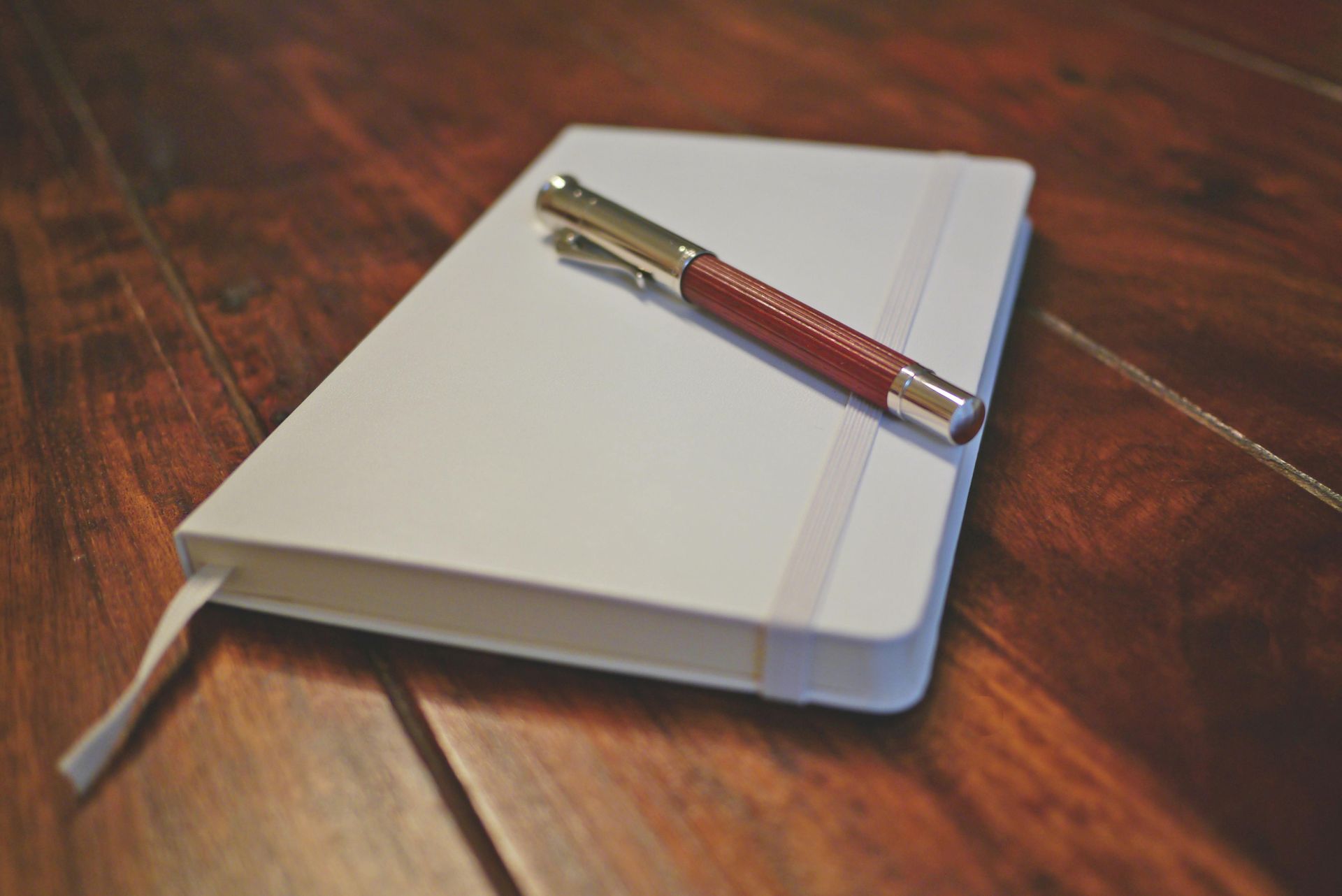 White notebook with a red pen on a dark wood table.