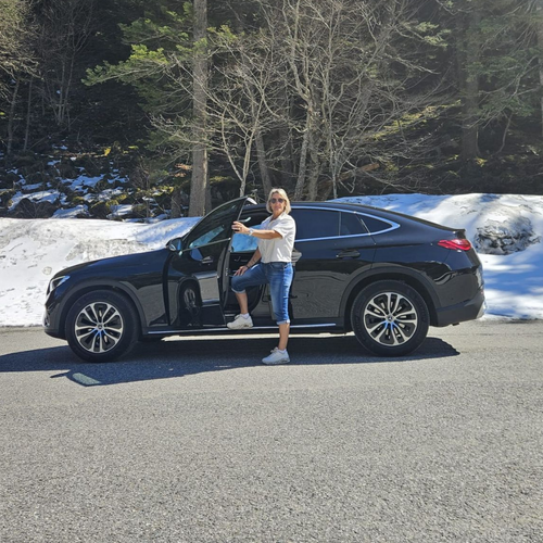 Une personne se tient près d'un SUV noir décapotable sur le bord d'une route enneigée, avec des arbres en arrière-plan.