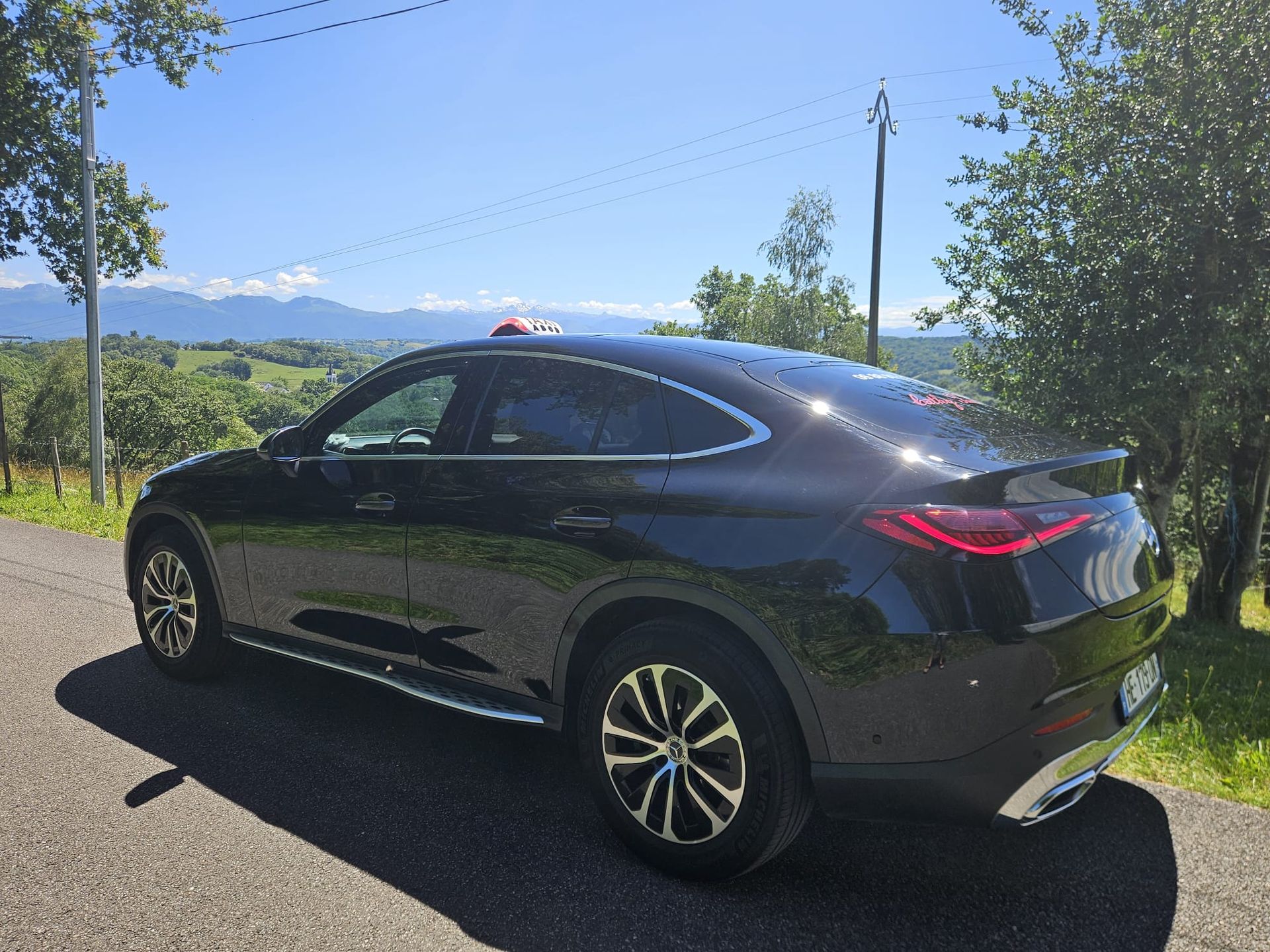 Un SUV noir sur une route de campagne bordée de champs, sous un ciel bleu azur.