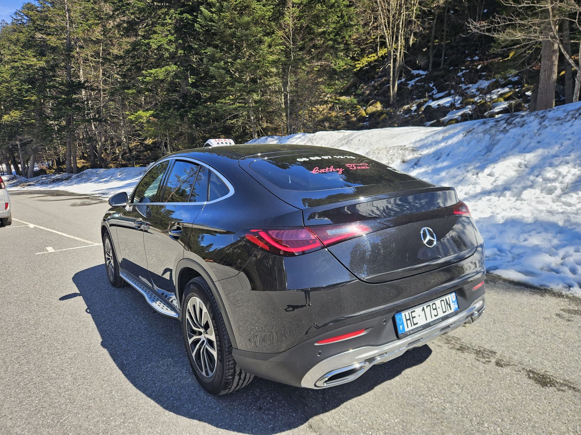 Un SUV Mercedes noir sur une route de montagne enneigée, bordée d'arbres.