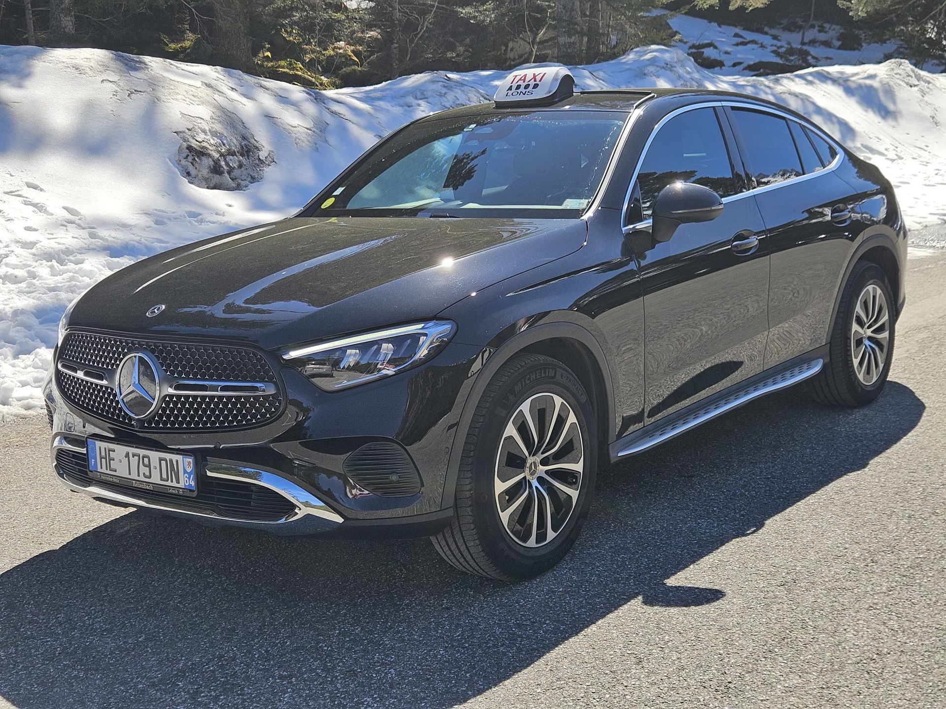 SUV Mercedes noir garé au bord d'une route enneigée, avec des montagnes en arrière-plan.