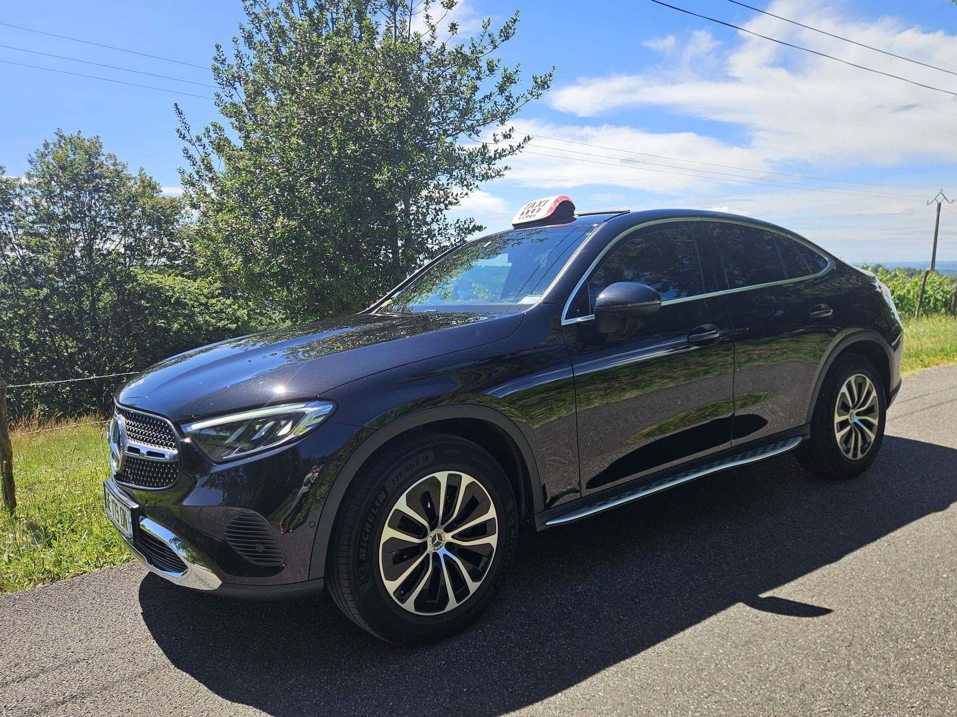 SUV noir garé au bord d'une route ensoleillée, sous des arbres et un ciel bleu.