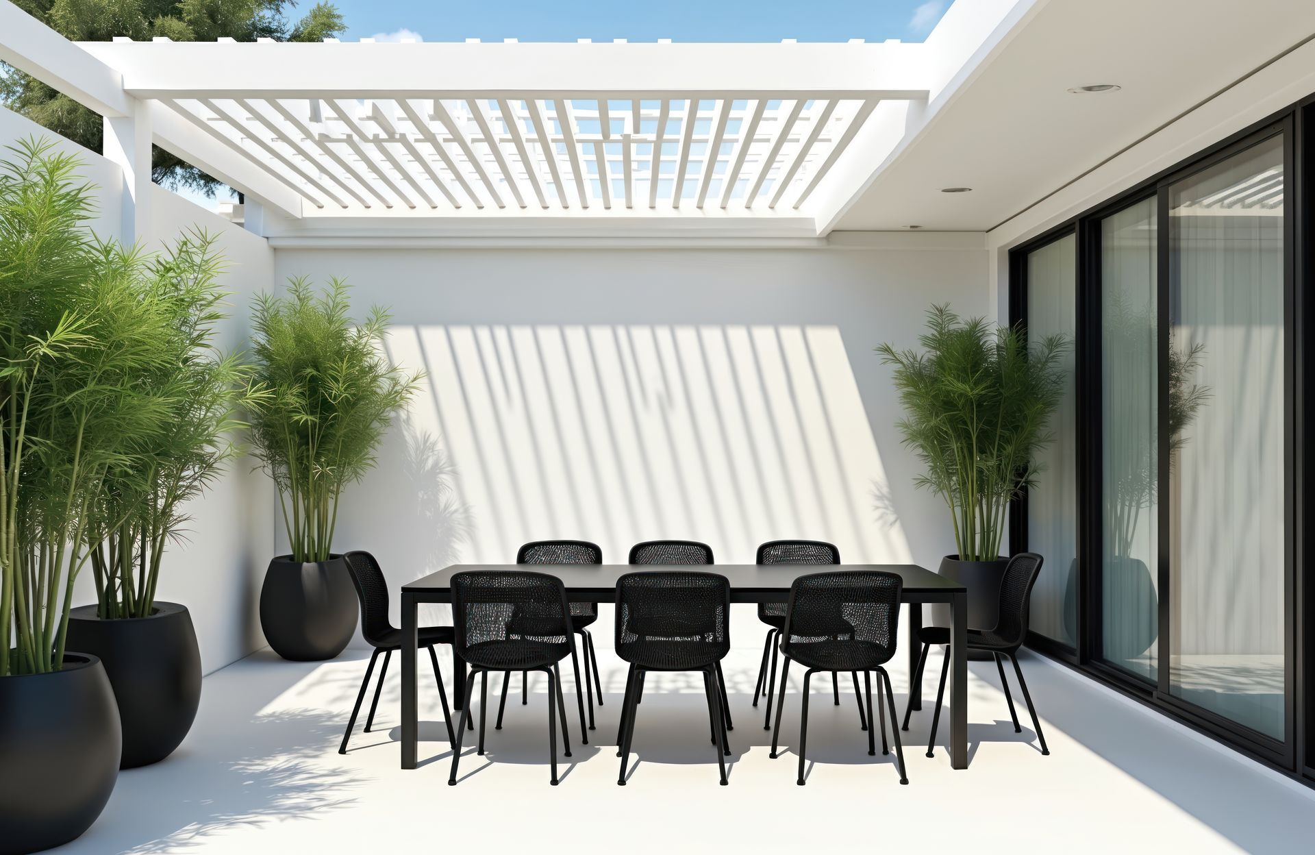 Coin repas extérieur avec table et chaises noires, plantes de bambou et pergola blanche.