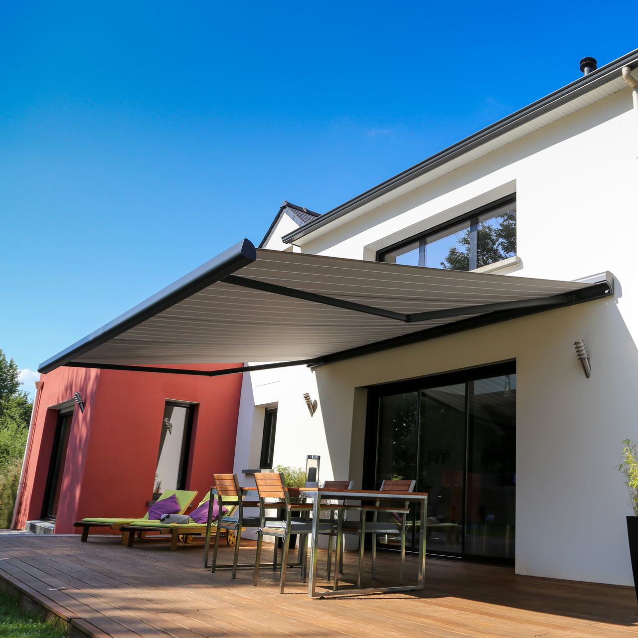 Une maison moderne avec un auvent rétractable au-dessus d'un coin repas extérieur, sous un ciel bleu.