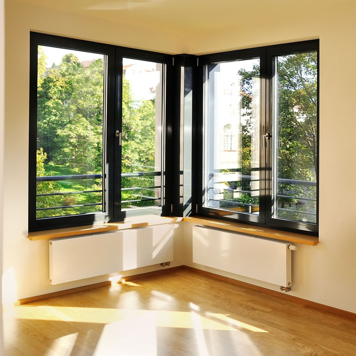 Fenêtres d'angle à cadres noirs, donnant sur un paysage verdoyant, et un radiateur blanc en dessous.