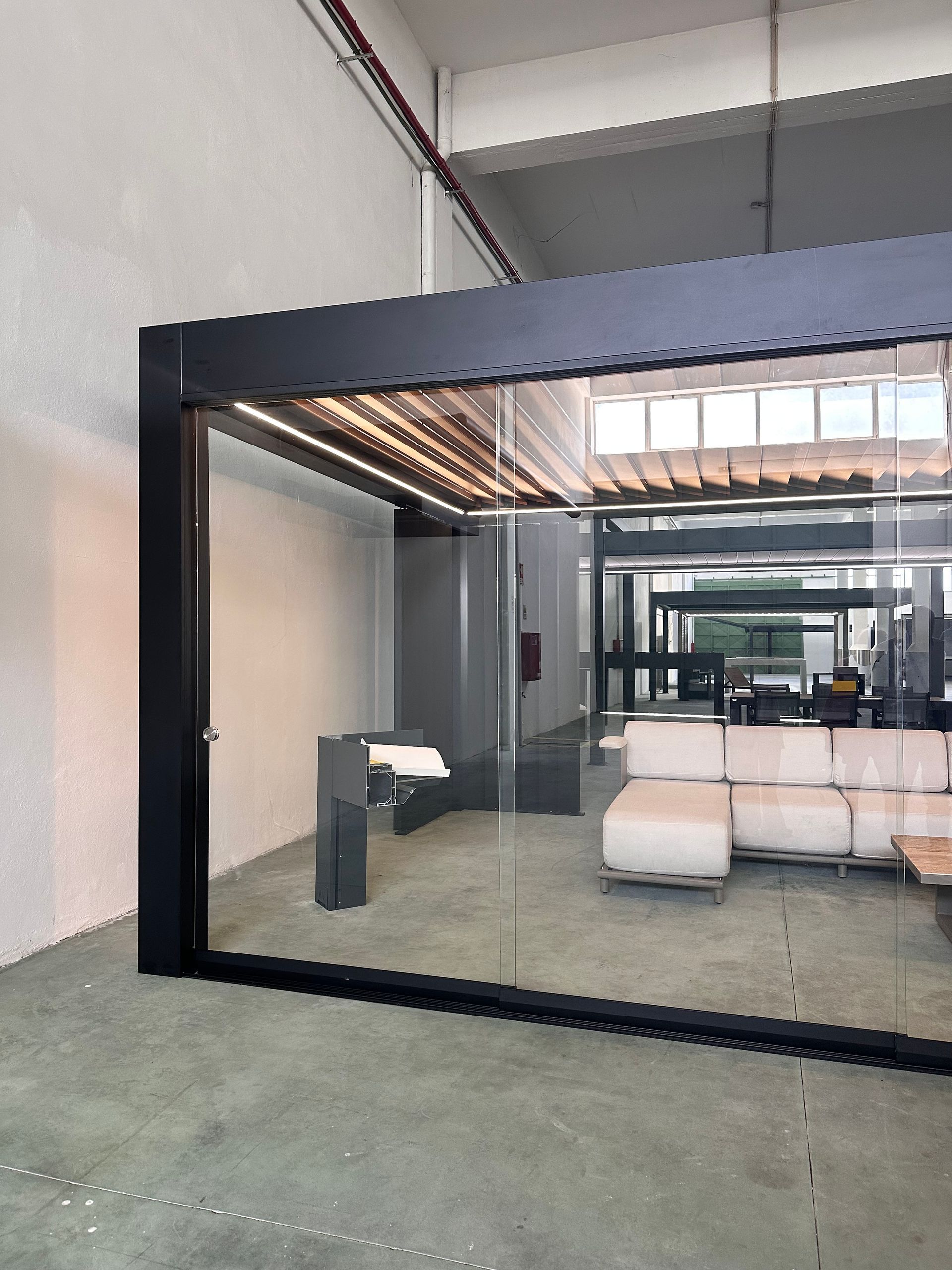 Structure extérieure moderne aux parois de verre, avec sièges, sol en béton.