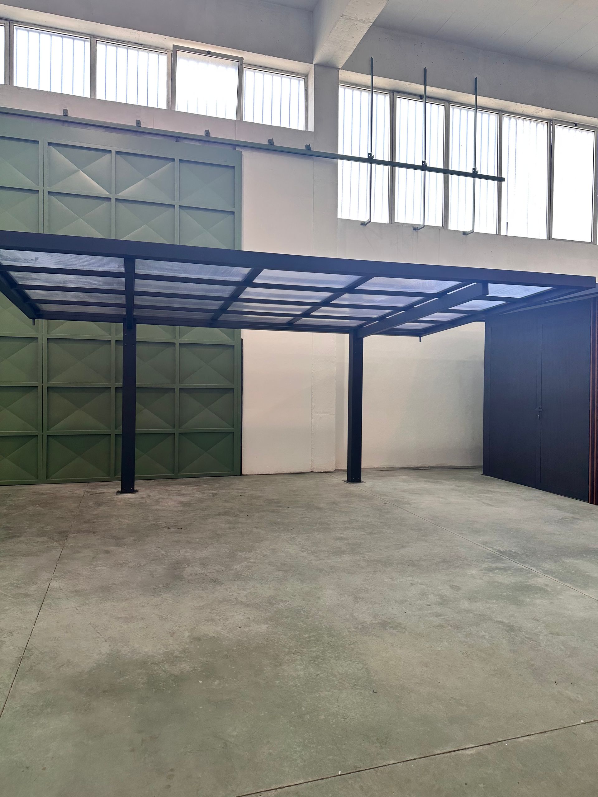 Abri de voiture métallique à l'intérieur d'un grand espace industriel avec panneaux de toit translucides et poteaux de soutien.