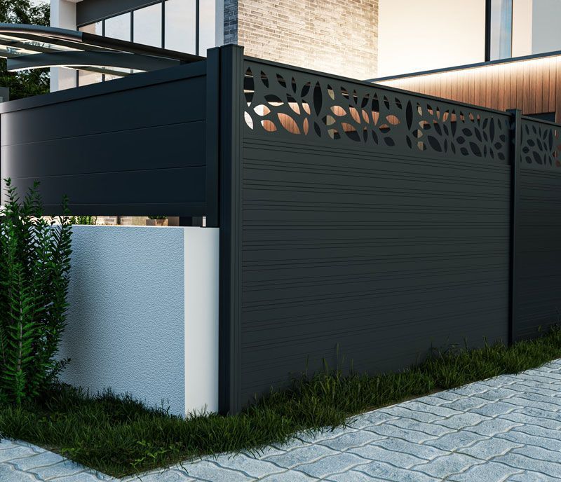 Clôture en métal noir ornée de découpes en forme de feuilles sur le dessus, se détachant sur un bâtiment moderne.