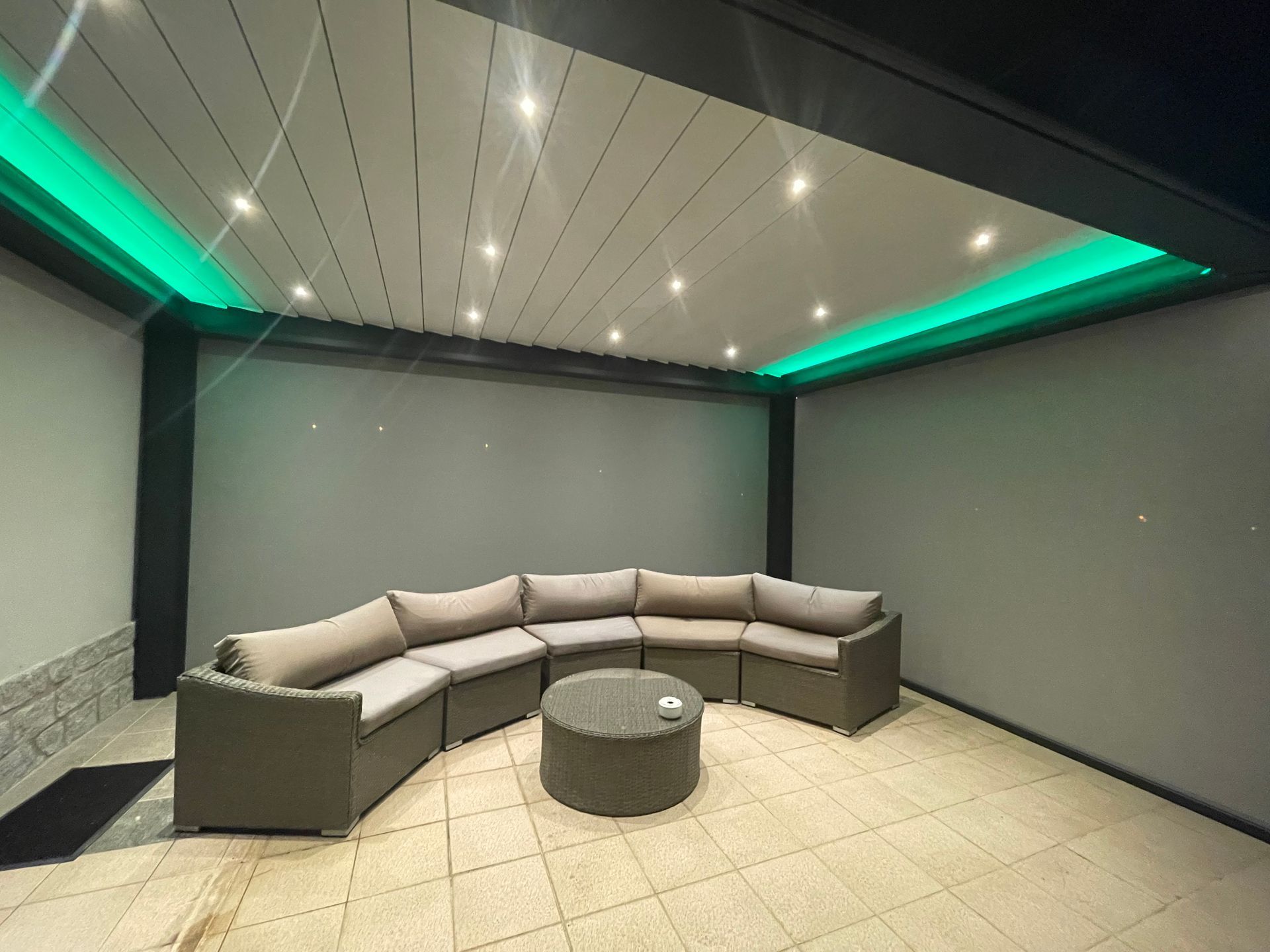 Salon de jardin avec canapé d'angle, table ronde et éclairage LED vert.