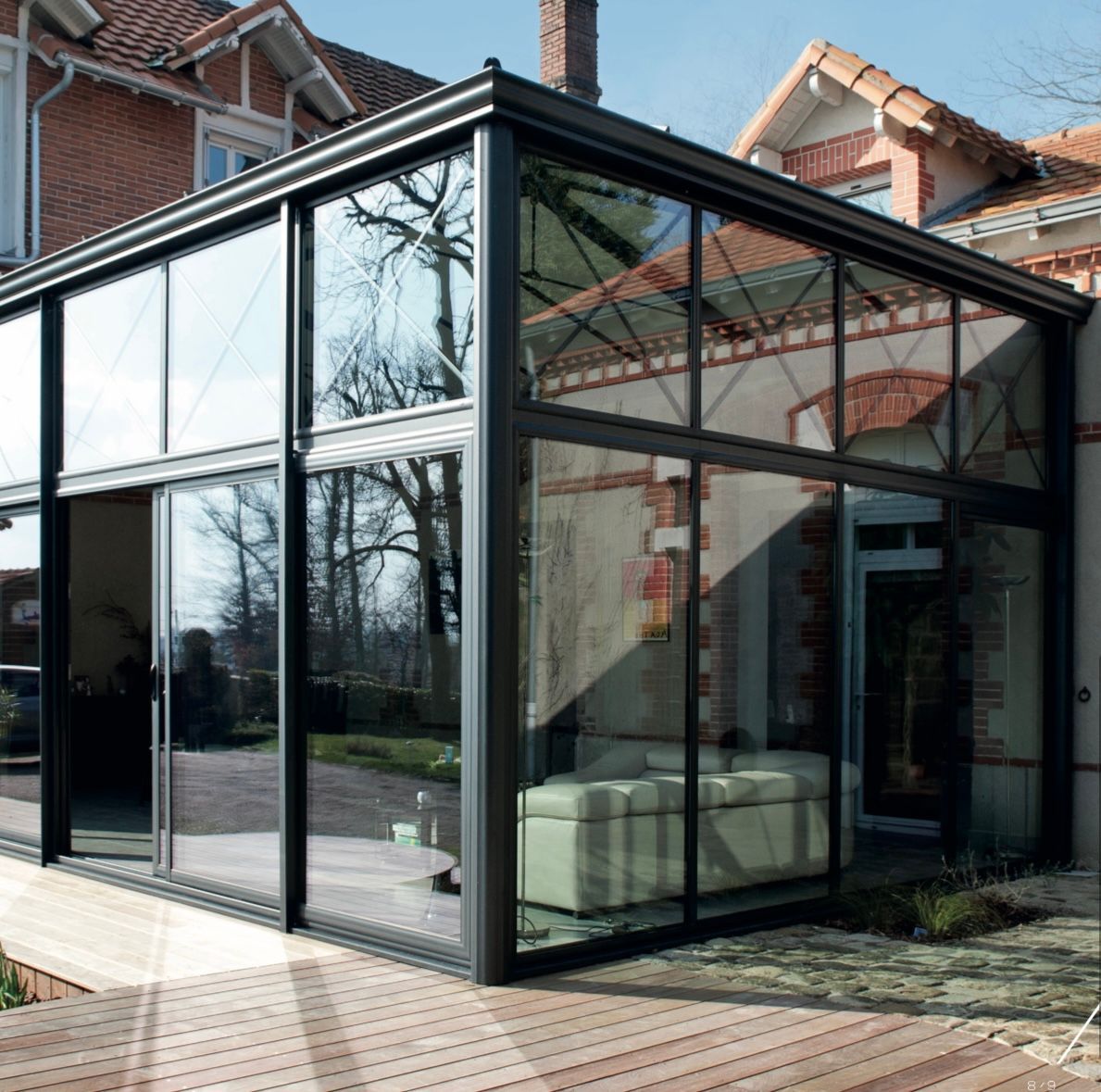 Extension d'une maison en briques comprenant une véranda vitrée, une porte coulissante en verre et un canapé à l'intérieur.