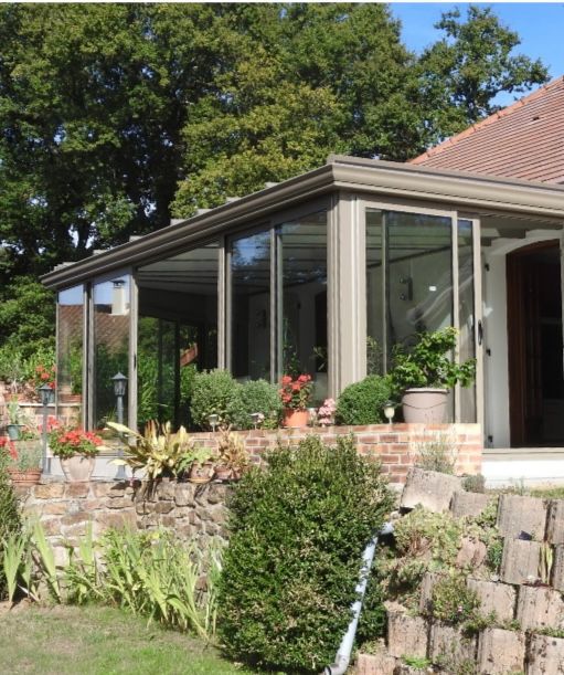 Extension de véranda vitrée sur une maison avec aménagement paysager en briques et en pierres.