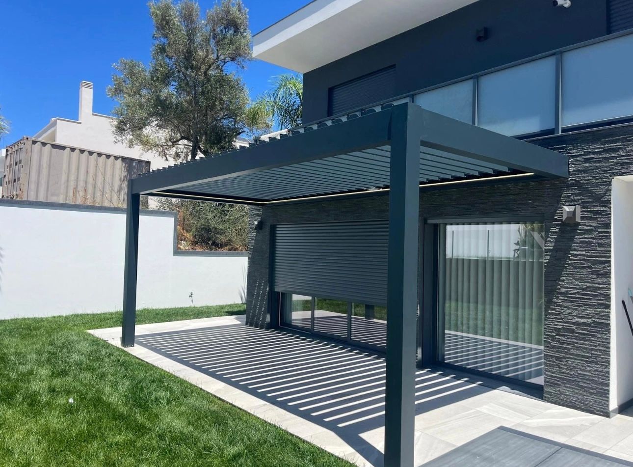 Une pergola moderne gris foncé projette une ombre à motifs sur la pelouse jouxtant une maison aux grandes fenêtres.