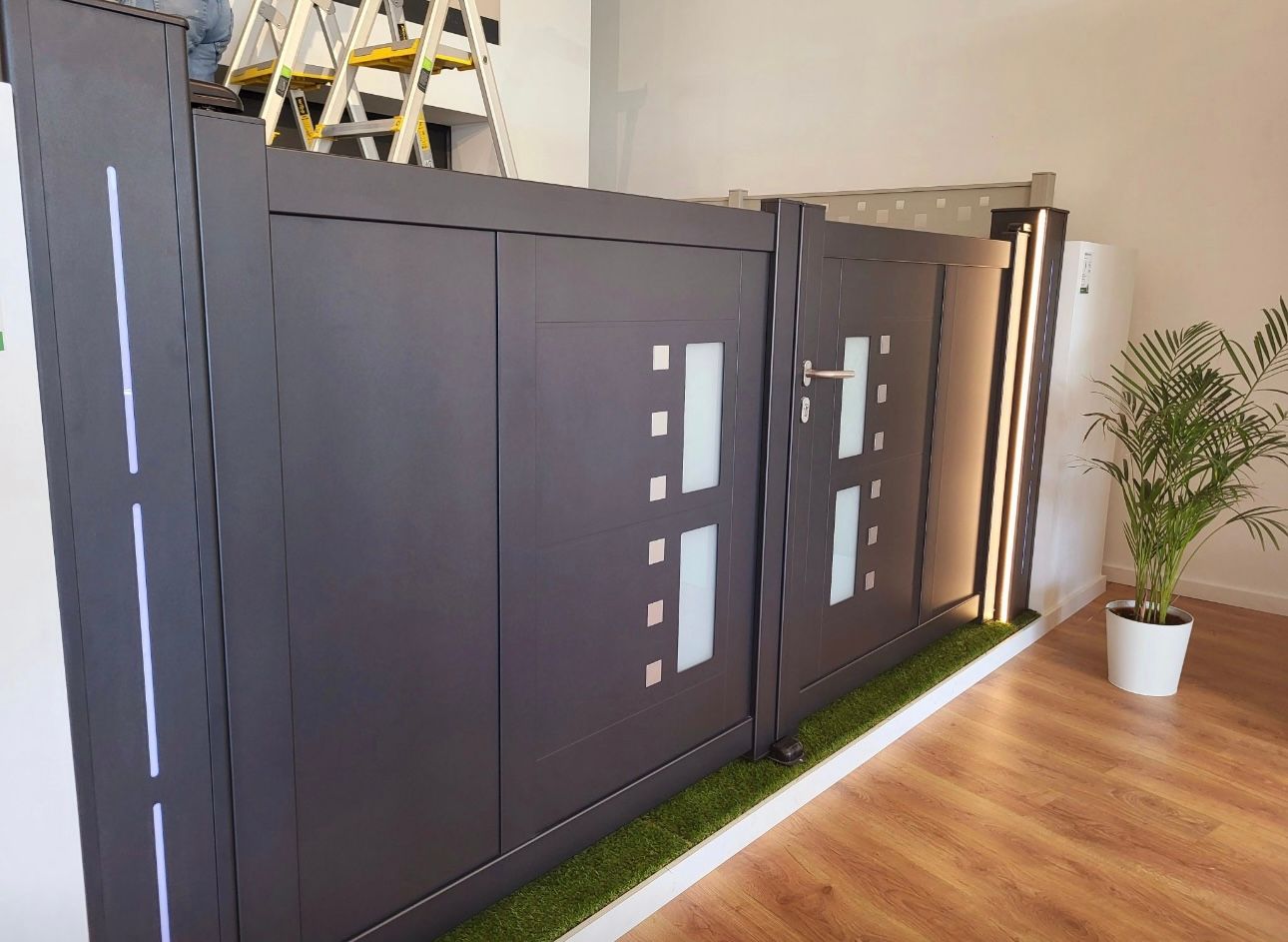 Portail moderne gris foncé avec éléments en verre, éclairage LED et gazon artificiel.