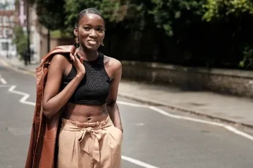 A woman in a black crop top and brown pants is standing on a street.