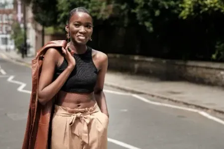 A woman in a black crop top and brown pants is standing on a street.