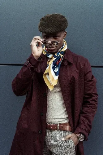 A man wearing a hat and scarf is standing in front of a wall.
