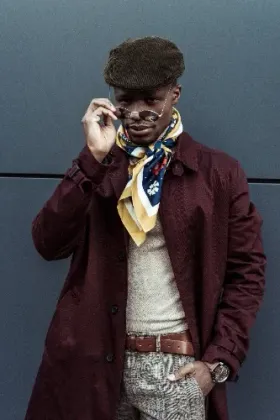 A man wearing a hat and scarf is standing in front of a wall.