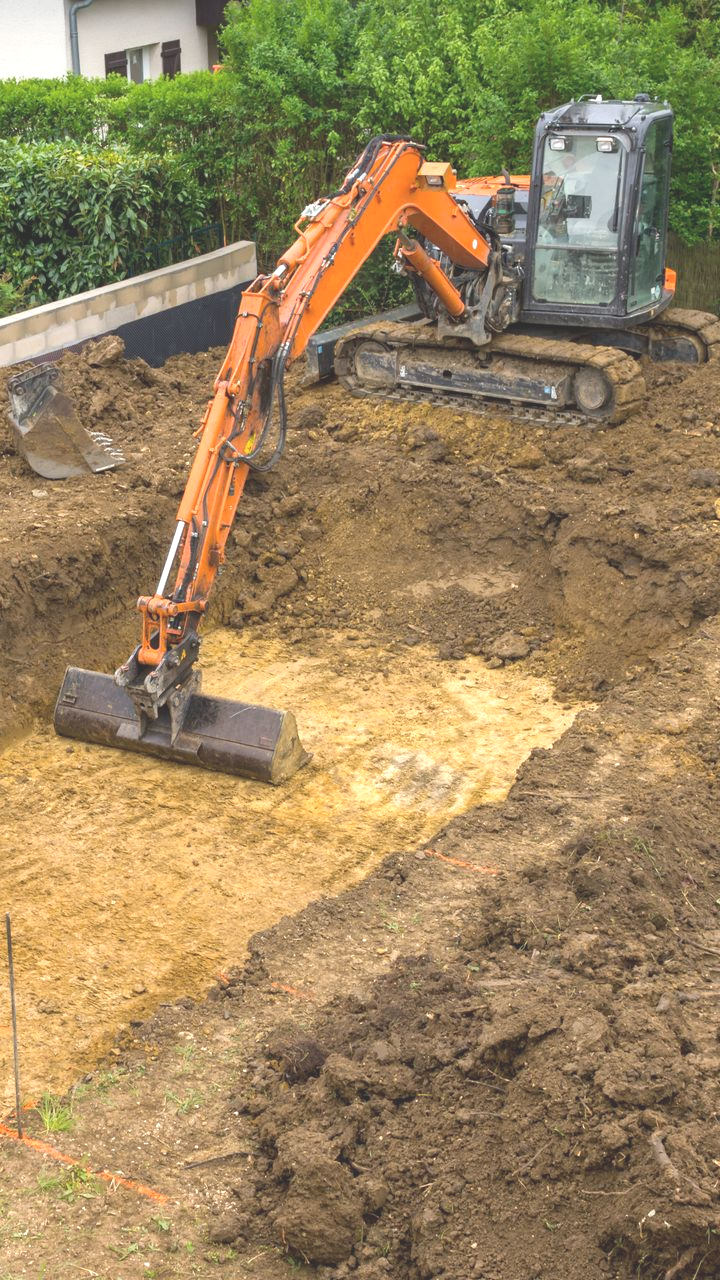 Une pelleteuse orange creuse dans une fosse à terre.