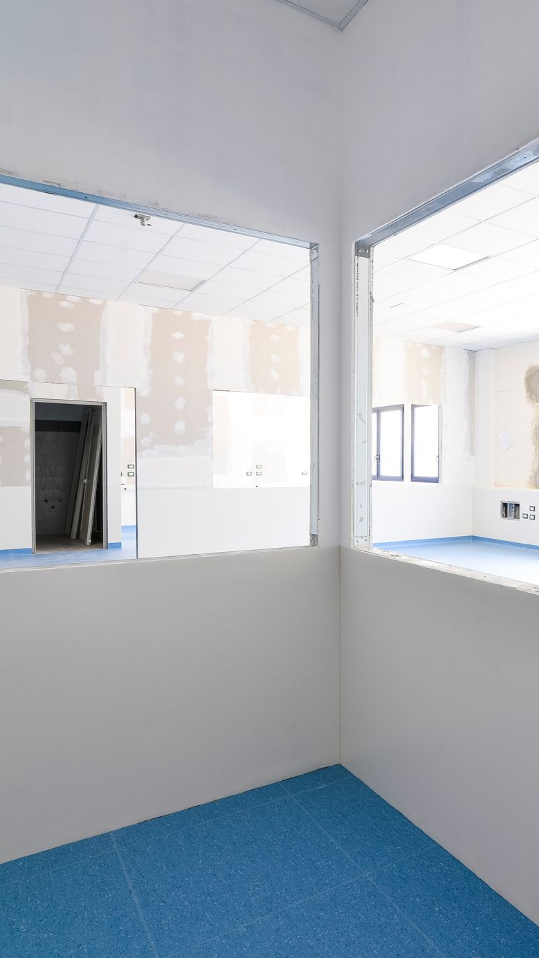 Intérieur d'une pièce en construction, avec un revêtement de sol bleu, des murs blancs et des fenêtres ouvertes.