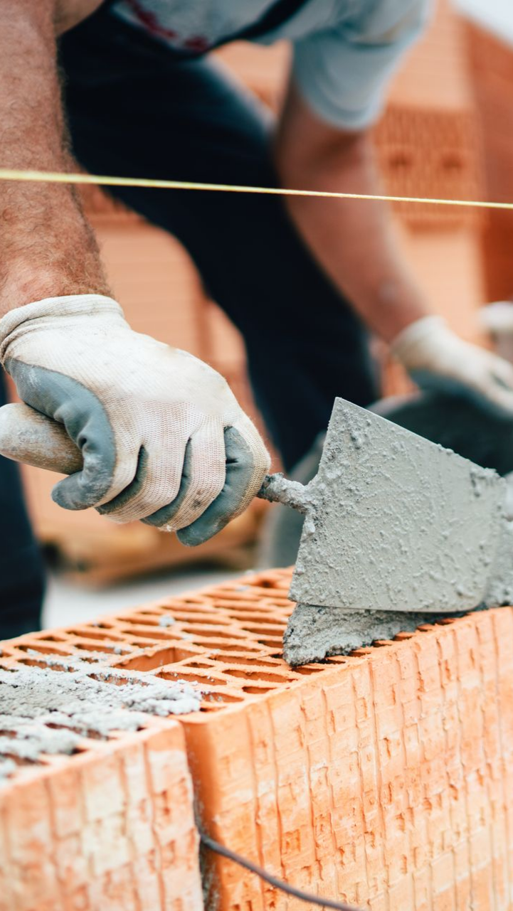 Ouvrier du bâtiment utilisant une truelle pour étaler du mortier sur des briques, en extérieur.