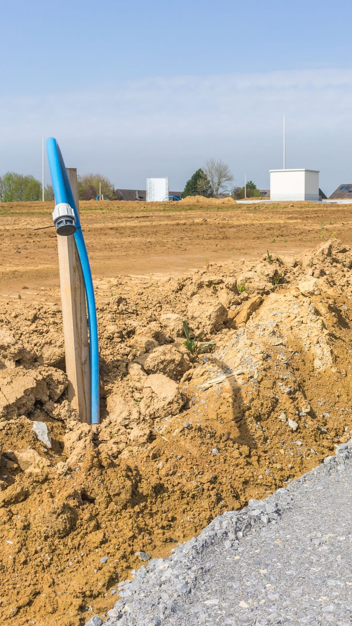 Tuyau bleu sortant d'une tranchée de terre. Chantier, plein jour.